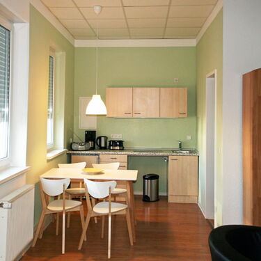 Moderne Küche mit Esstisch, vier Stühlen und hölzernen Schränken auf glänzendem Holzboden im gemütlichen Ambiente.