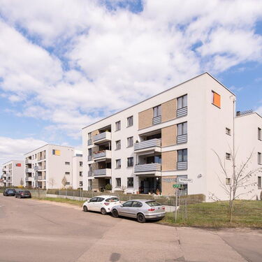 Mehrfamilienhäuser mit Balkonen stehen an einer ruhigen Straßenecke unter einem klaren blauen Himmel.