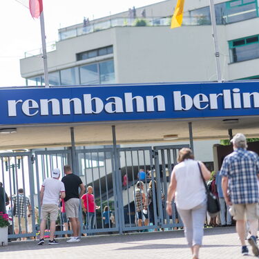 Besucher strömen zur Rennbahn Berlin, um an einem sonnigen Tag die Atmosphäre des Pferderennens zu genießen.