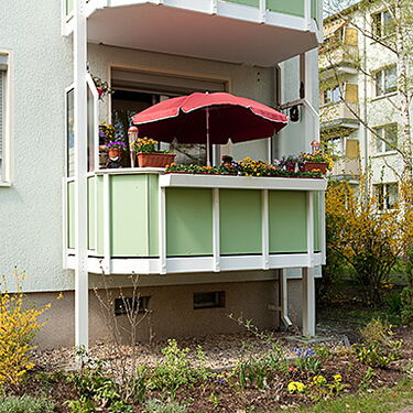 Ein Balkon mit roten Sonnenschirm und bunten Blumen in einer Wohnsiedlung bietet eine gemütliche Atmosphäre.