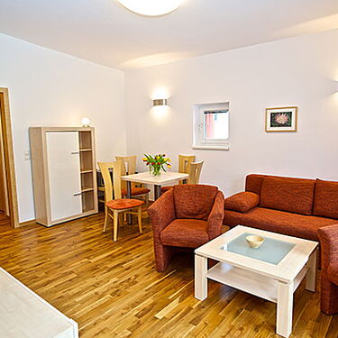 Ein gemütliches Wohnzimmer mit roten Sofas, Holzboden und einem Esstisch verleiht dem Waschhaus eine einladende Atmosphäre.