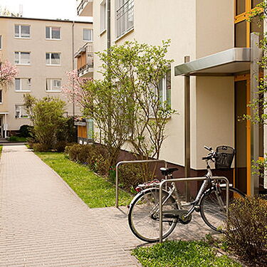 Ein Fahrrad steht vor einem modernen Wohnhaus, umgeben von blühenden Bäumen und gepflegtem Grün in einer Wohnanlage.