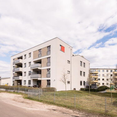 Mehrstöckige Wohngebäude mit Balkonen und einem kleinen Spielplatz im Hof an einem bewölkten Tag.