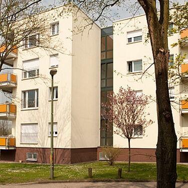 Ein modernes Wohngebäude mit gelben Balkonen steht umgeben von Bäumen und Grünflächen im Wuhleblick.