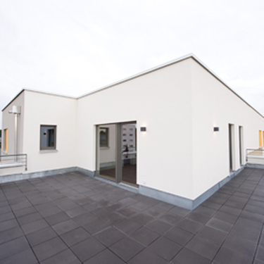 Die großzügige Terrasse eines Neubaus zeigt eine moderne, minimalistische Gestaltung mit grauen Bodenfliesen.