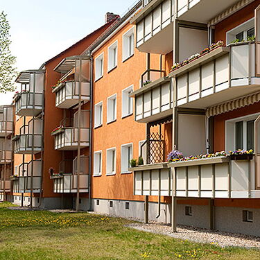 Mehrfamilienhäuser mit orangefarbener Fassade und Balkonen stehen entlang einer grünen Rasenfläche.