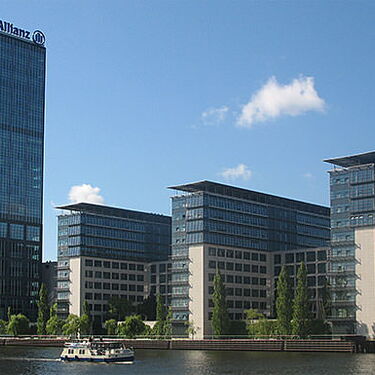 Ein Boot fährt auf einem Fluss vor modernen Hochhäusern in Köpenick entlang, die sich im Wasser spiegeln.
