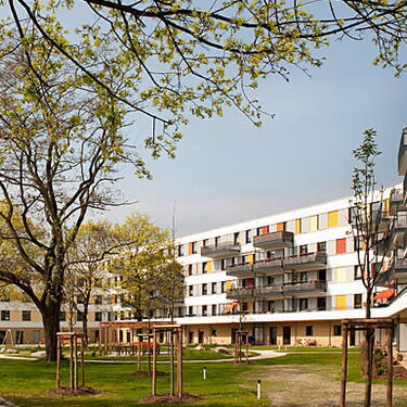 Mehrstöckige Wohngebäude mit bunten Balkonen umgeben einen grünen Innenhof im Wuhlebogen-Viertel.