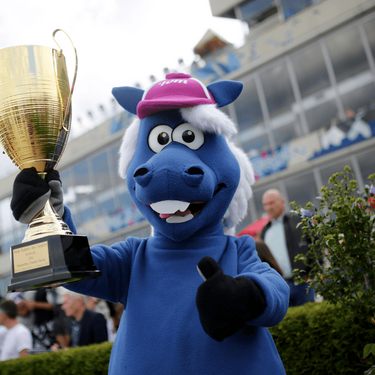 Der Maskottchen Tippel Tom hält jubelnd den Siegerpokal bei einer Veranstaltung in einer festlichen Atmosphäre.
