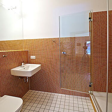 Ein modernes Badezimmer mit roten Fliesen zeigt eine Glasdusche, ein Waschbecken und eine Toilette.