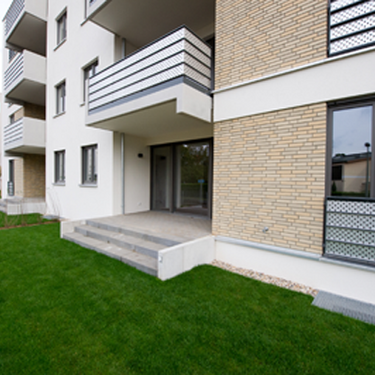 Ein moderner Neubau mit Balkonen und gepflegtem Gartenbereich erstreckt sich entlang des Gebäudes.