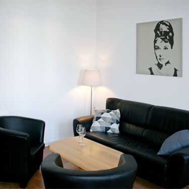 Ein gemütliches Wohnzimmer mit schwarzem Ledersofa, zwei Sesseln, einem Couchtisch und einem Porträt an der Wand.