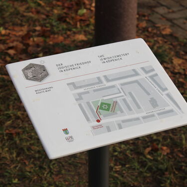 Eine Informationstafel zeigt eine Karte des Jüdischen Friedhofs in Köpenick, umgeben von herbstlichem Laub.