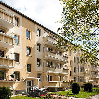 Mehrstöckige Wohngebäude mit Balkonen und gepflegten Grünflächen an einem sonnigen Tag.