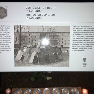 Eine Informationstafel beschreibt den jüdischen Friedhof in Köpenick, umgeben von brennenden Kerzen.