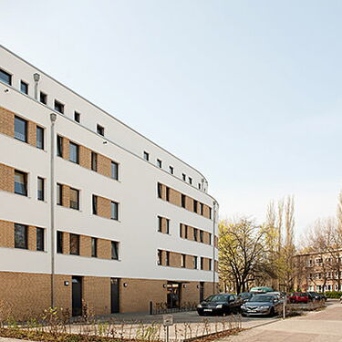 Ein modernes Wohngebäude mit weißen und ziegelroten Fassaden steht an einer ruhigen Straße im Wuhlebogen-Viertel.