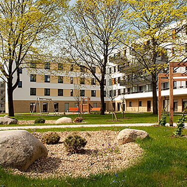 Ein moderner Wohnkomplex umgeben von Bäumen und gepflegten Grünflächen unter einem sonnigen Himmel im Wuhlebogen.