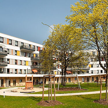 Ein modernes Wohngebäude mit bunten Balkonen steht umgeben von gepflegten Gärten und Bäumen im Wuhlebogen.