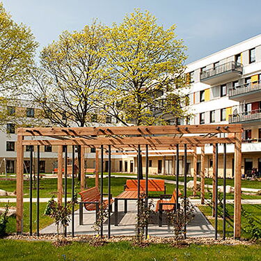 Ein moderner Innenhof mit Sitzbereich und Pergola, umgeben von Wohngebäuden und grünen Bäumen im Wuhlebogen.