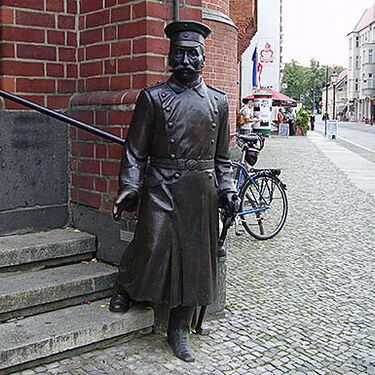 Eine bronzene Statue eines historischen Soldaten steht neben einer Treppe auf einer gepflasterten Straße in Köpenick.